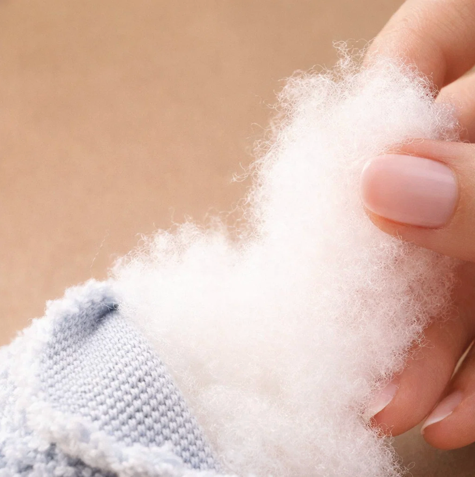 Hand holding a small ball of white cotton wool against a beige background